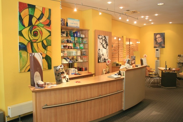 Moderner Optikerladen mit gelben Wänden, Brillenregalen und Beratungstheke im Verkaufsraum.